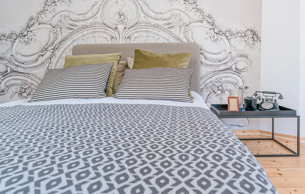 Un dormitorio con ropa de cama estampada y una pared decorativa ornamentada detrás de la cama.