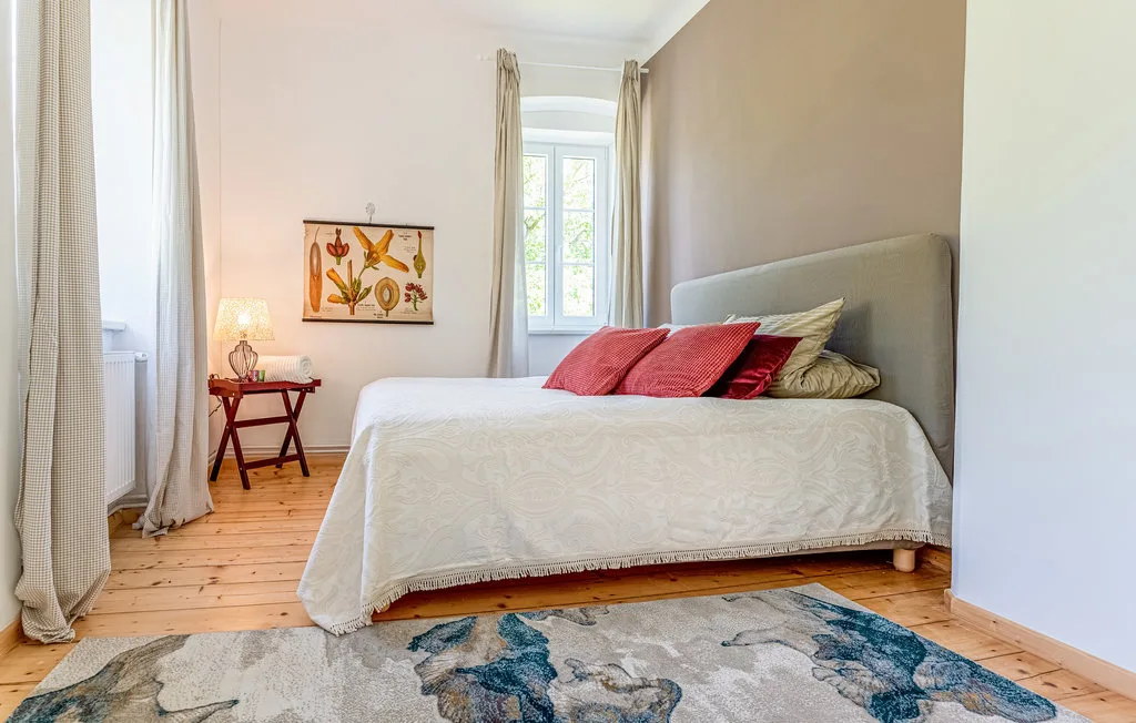 Un dormitorio con una cama, cojines de colores y ventanas altas con cortinas.