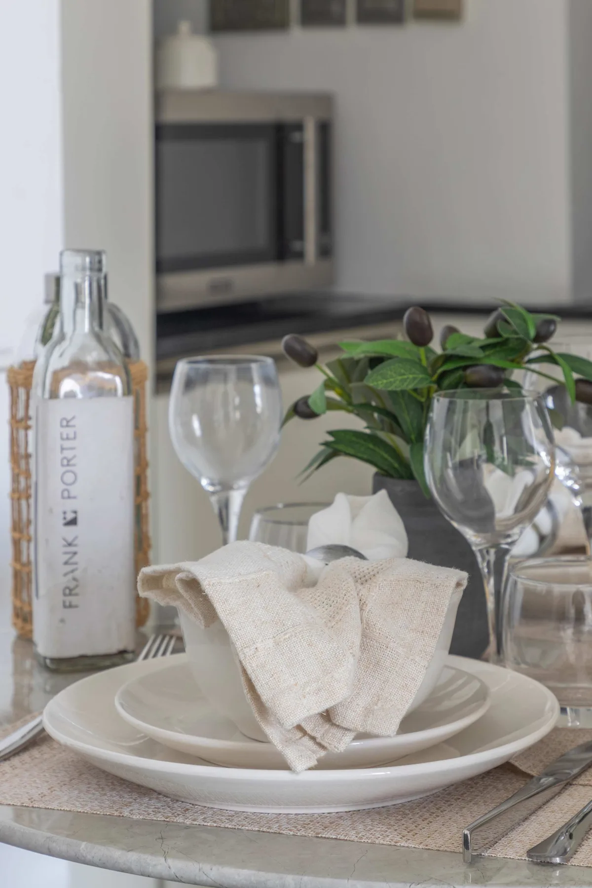 Una mesa de comedor está puesta con platos, servilletas dobladas, copas y una botella.