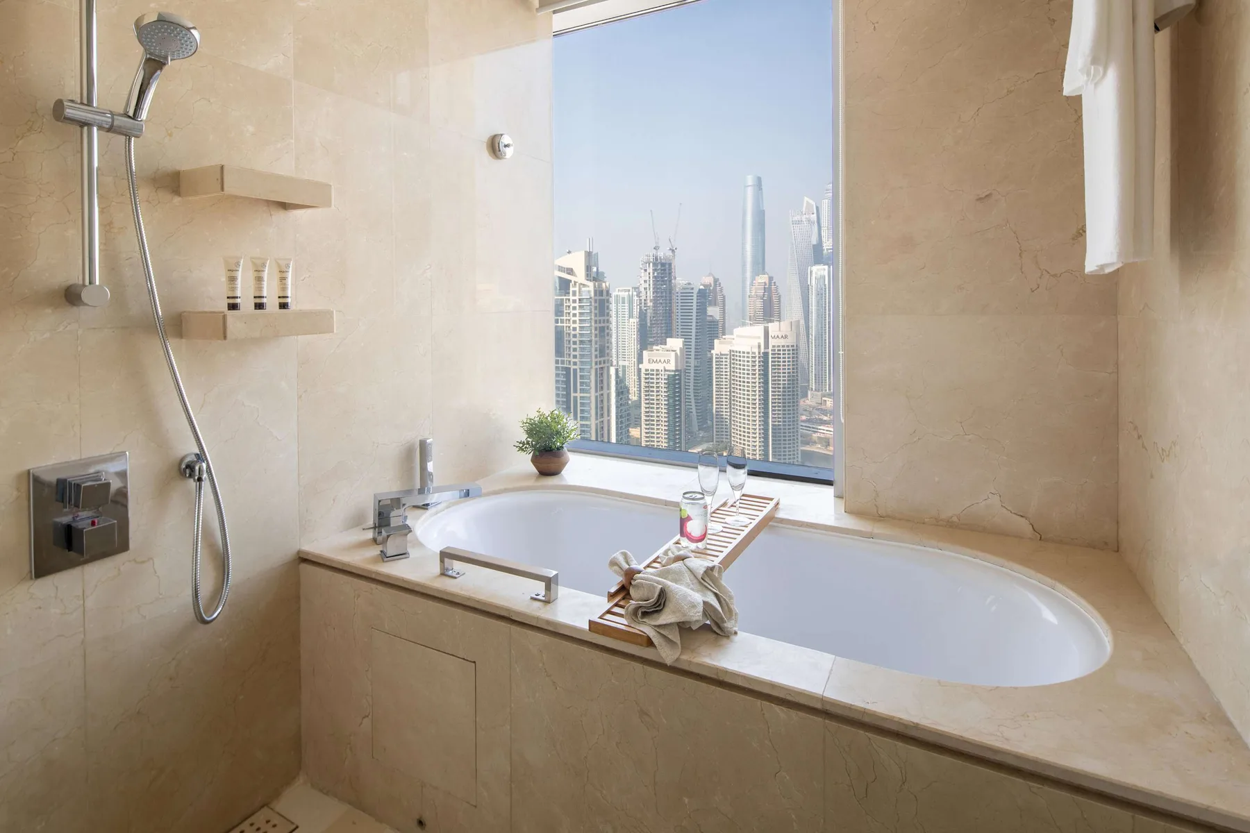 Un baño con una bañera empotrada junto a una ventana amplia con edificios de la ciudad a la vista.