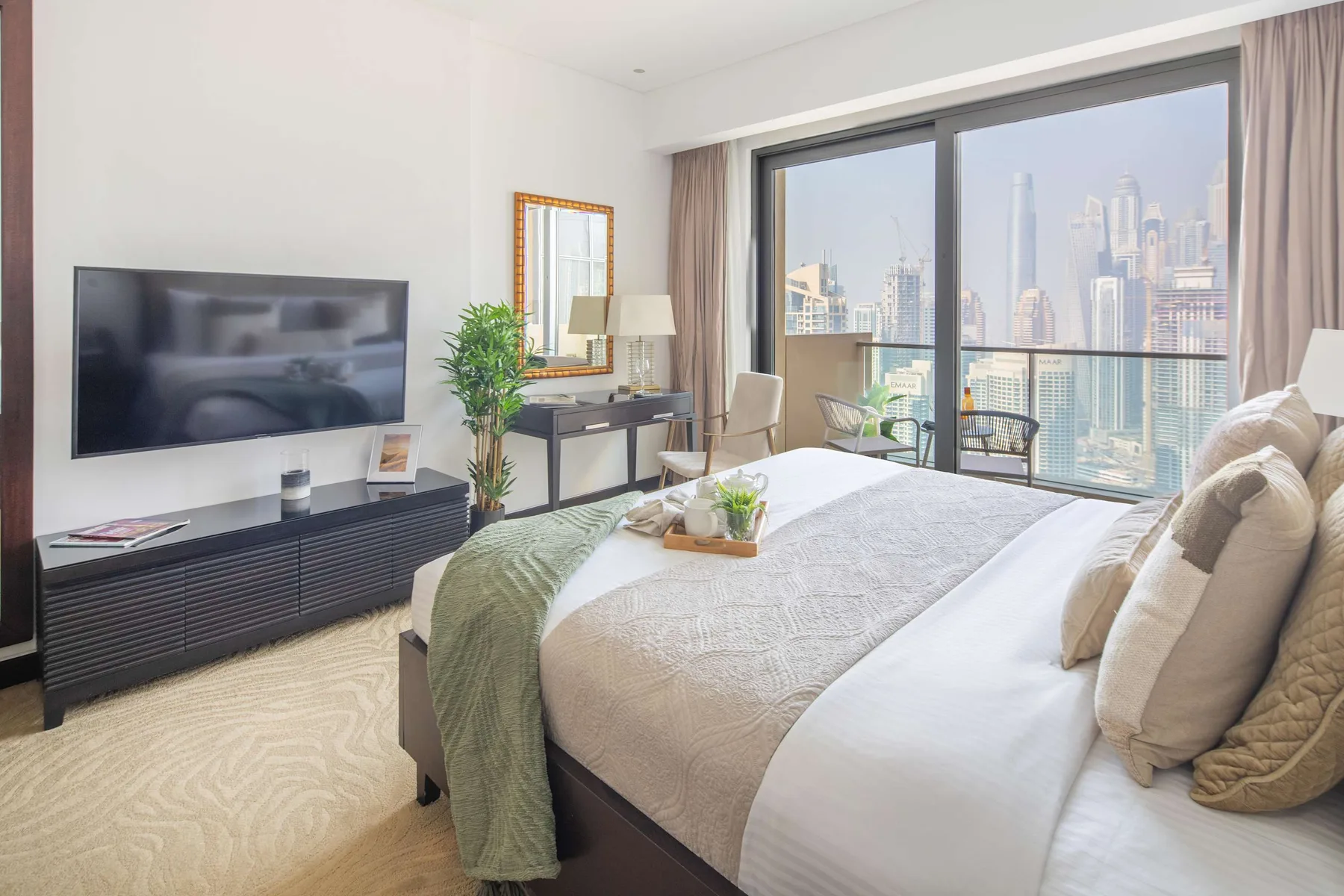 Un dormitorio luminoso con una cama grande junto a ventanales con vistas a la ciudad.