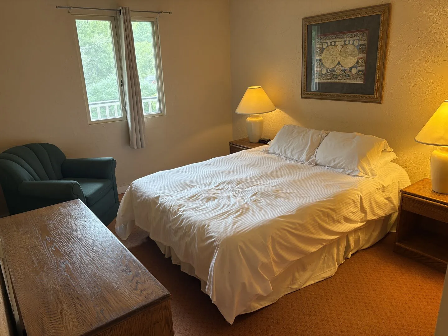 Un dormitorio con una cama grande, lámparas de noche y una silla junto a la ventana.
