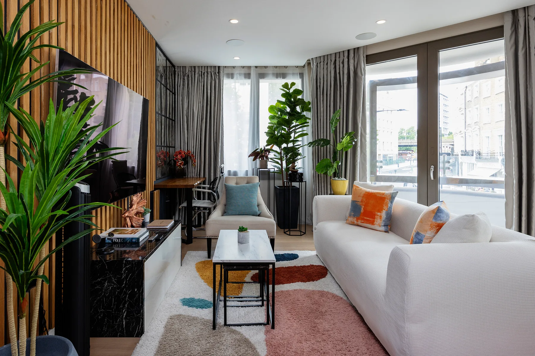 A bright living room with seating, a coffee table, plants, and large windows.