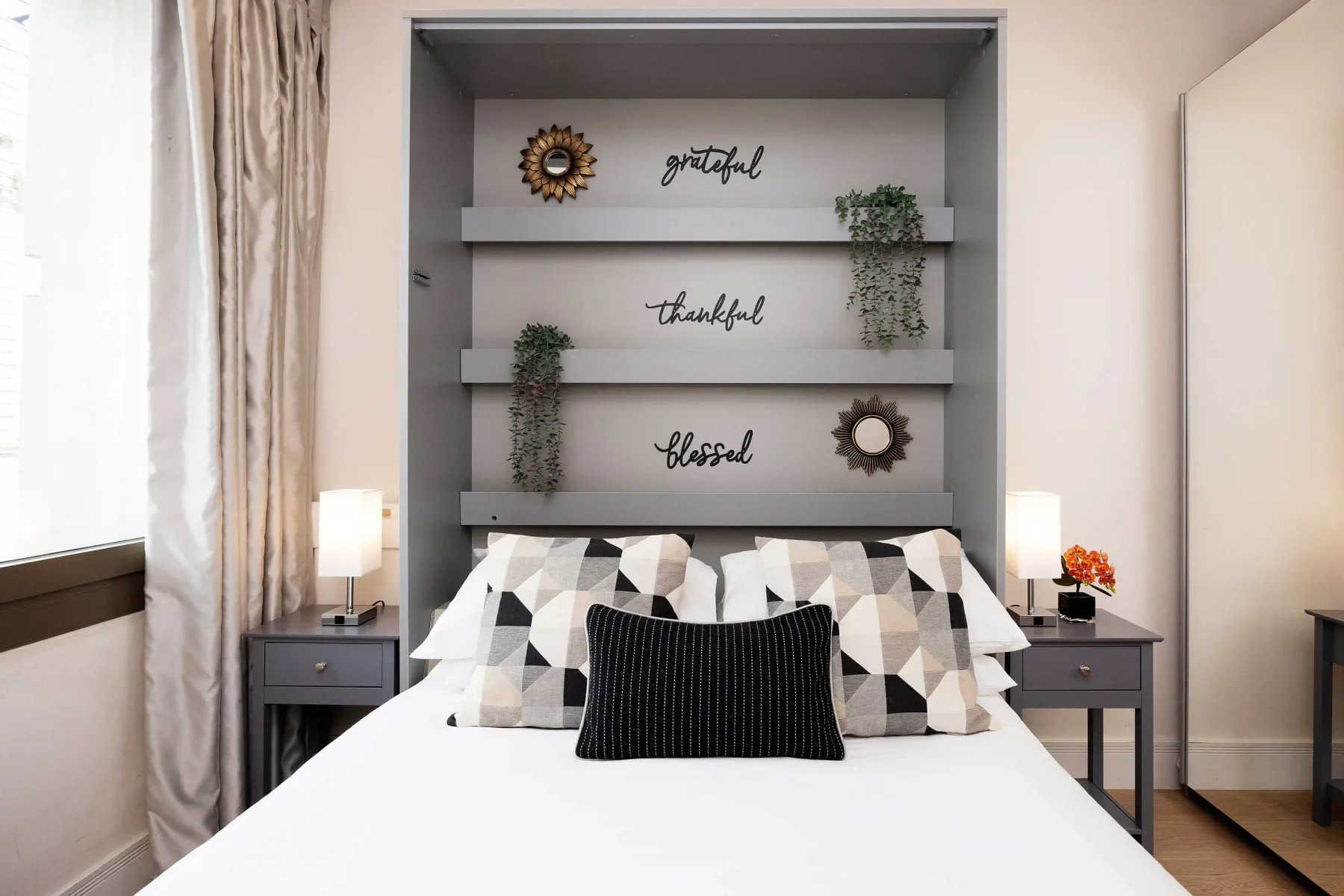 A bedroom with a neatly made bed and decorative recessed shelves behind it.