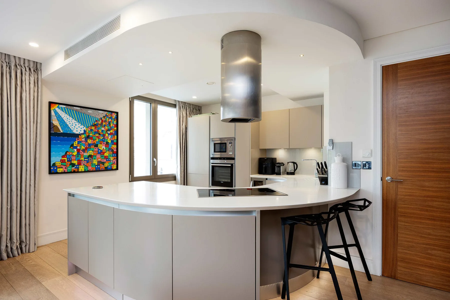 A bright modern kitchen with a curved island, bar seating, and colorful wall art.