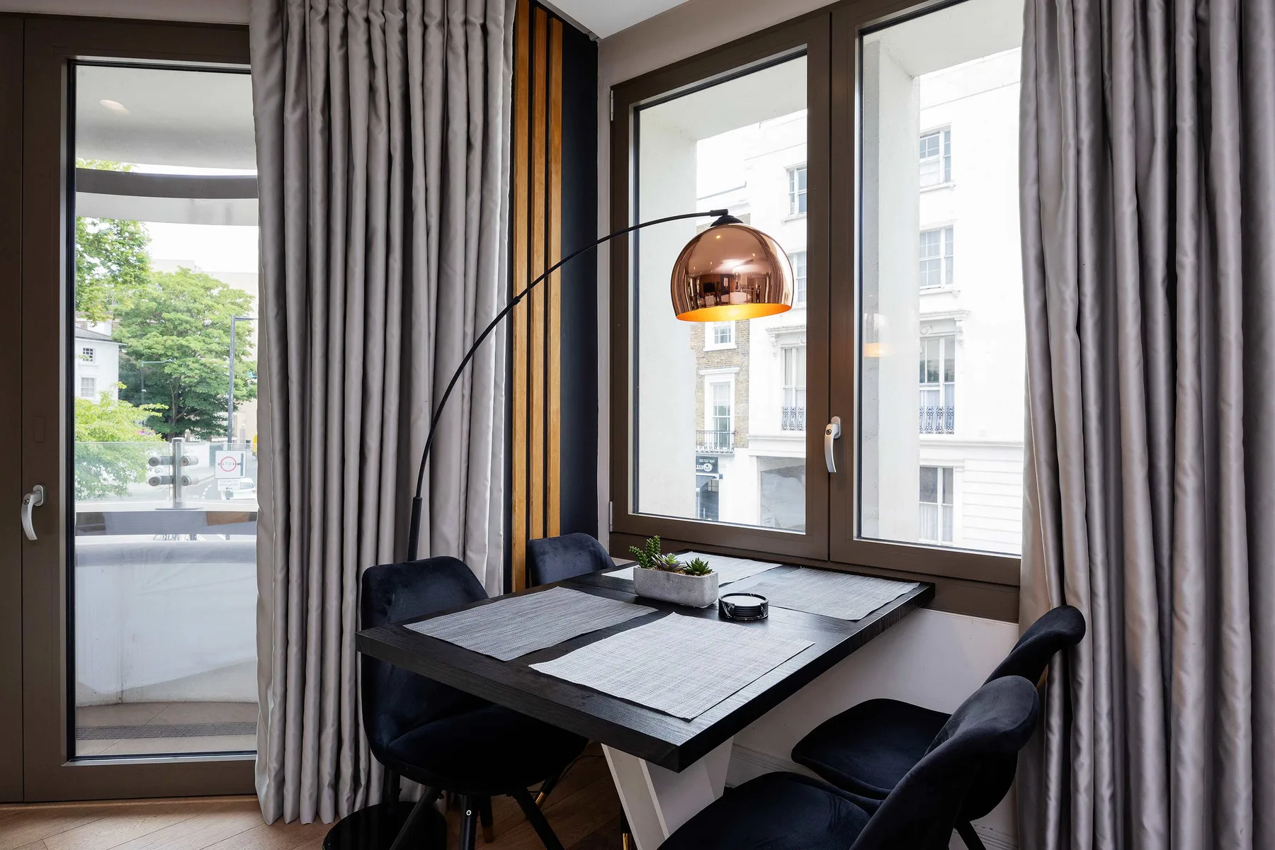 A dining area with a rectangular table and dark seating beside large windows.