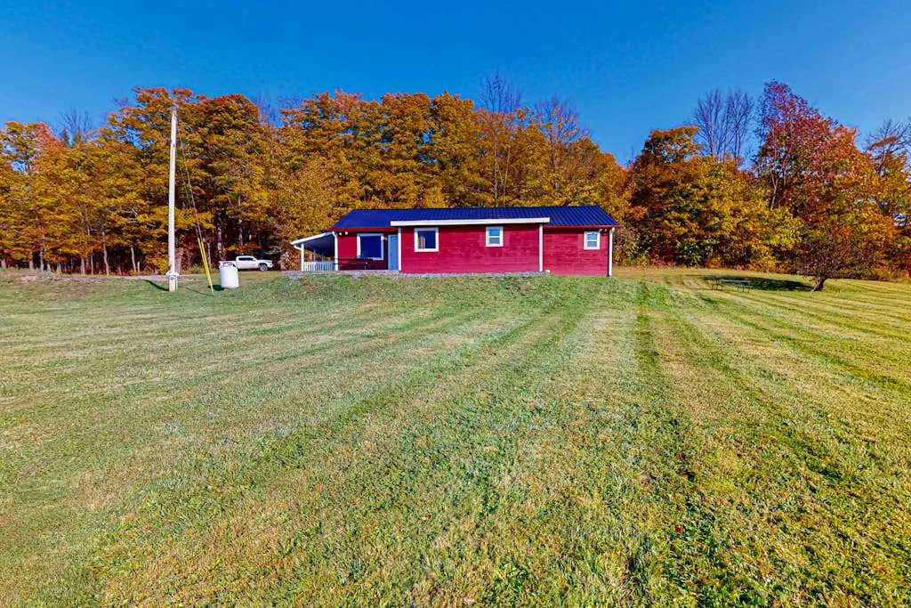 A red building stands beyond a broad grassy lawn, with autumn trees in the background.