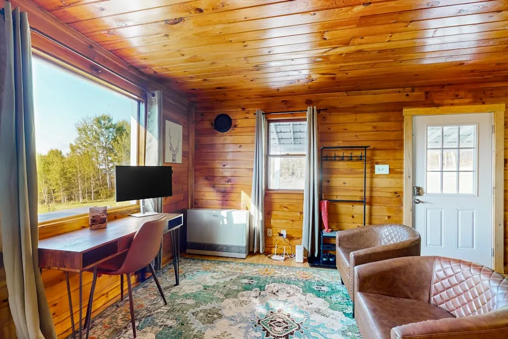 A wood-paneled living room with a desk beside a large window and seating.