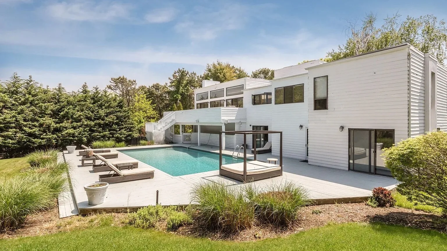 Una casa blanca moderna da a una piscina y una terraza exterior.