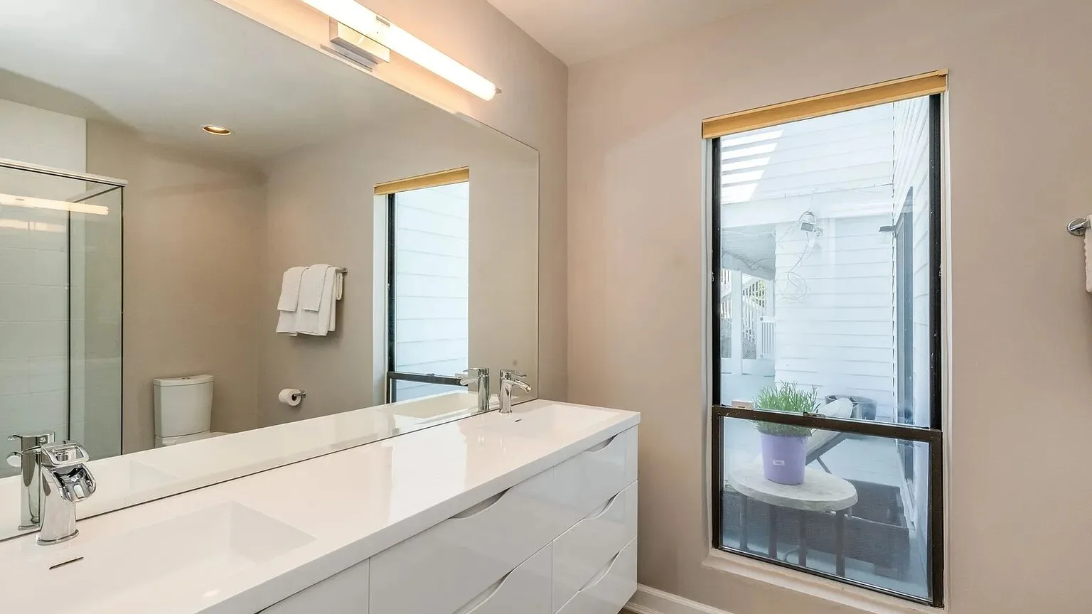 Un tocador de baño con un espejo amplio y una ventana alta.