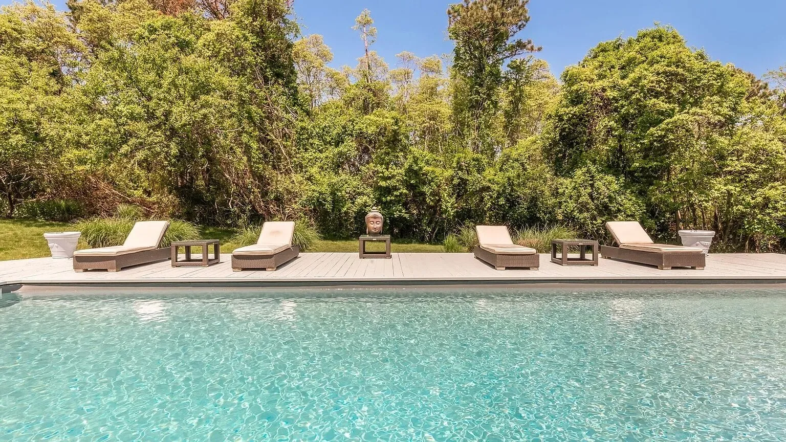 Una piscina bordeada por asientos reclinables y árboles frondosos.