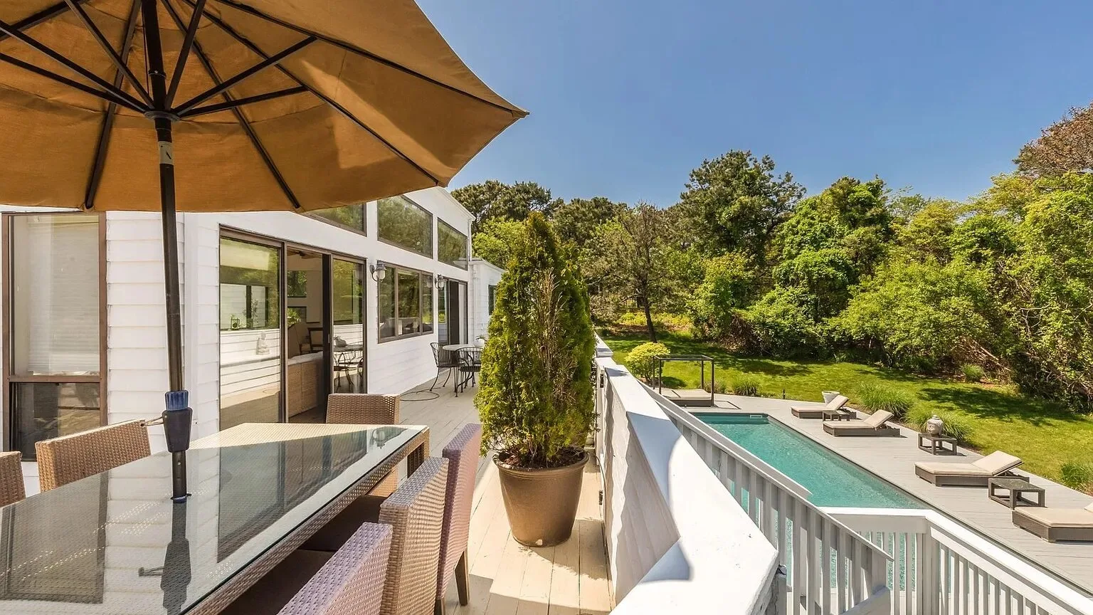 Un patio soleado con asientos, una sombrilla y una piscina junto a la casa.