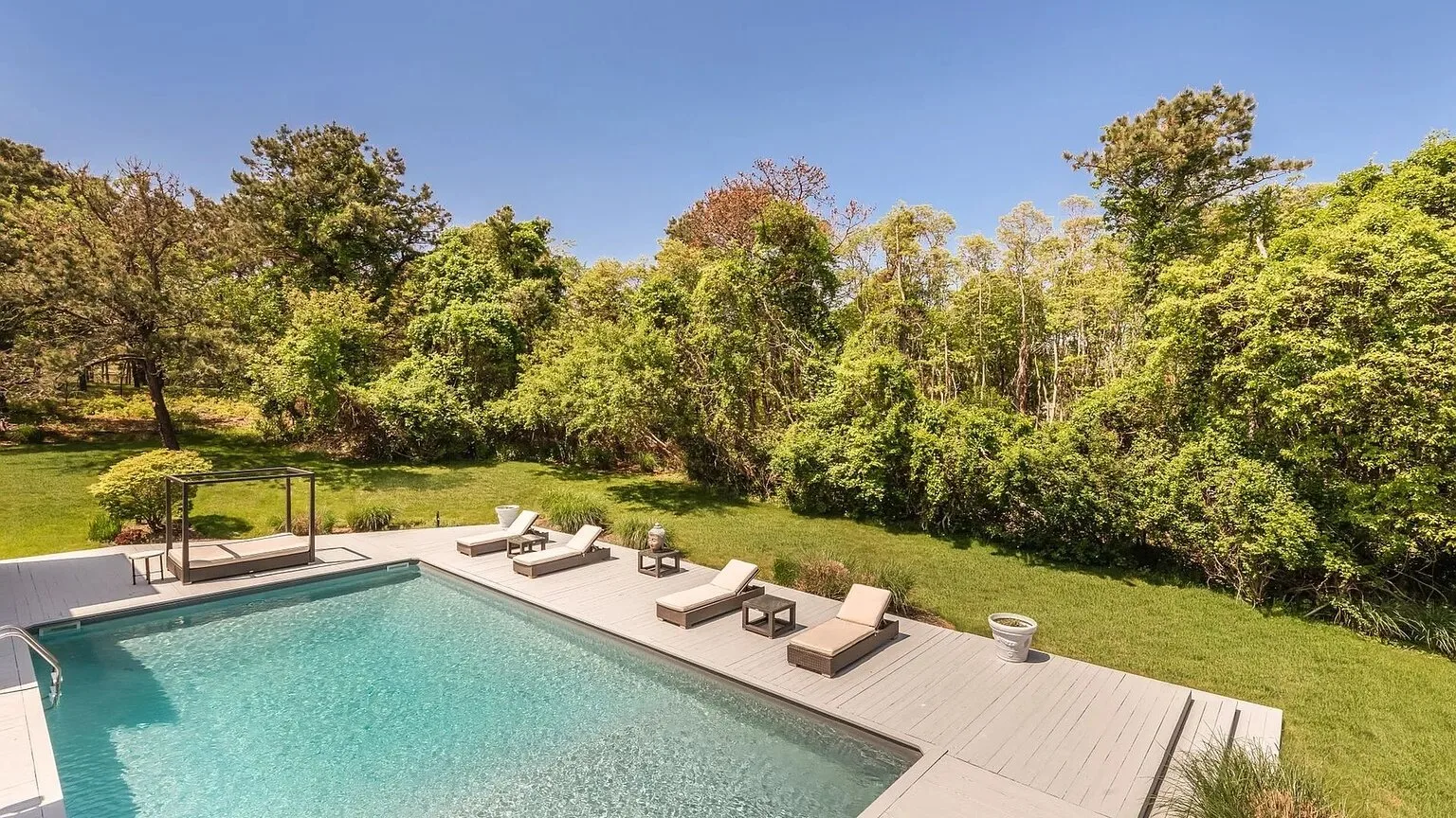 Una piscina al aire libre está junto a una terraza de madera, con árboles al fondo.