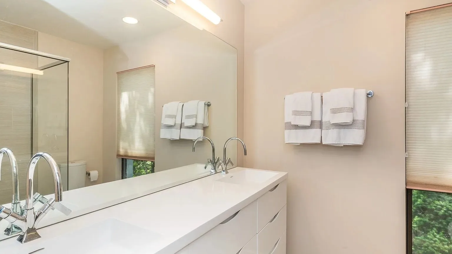 Un tocador de baño con una encimera larga, un espejo de pared y toallas dobladas.