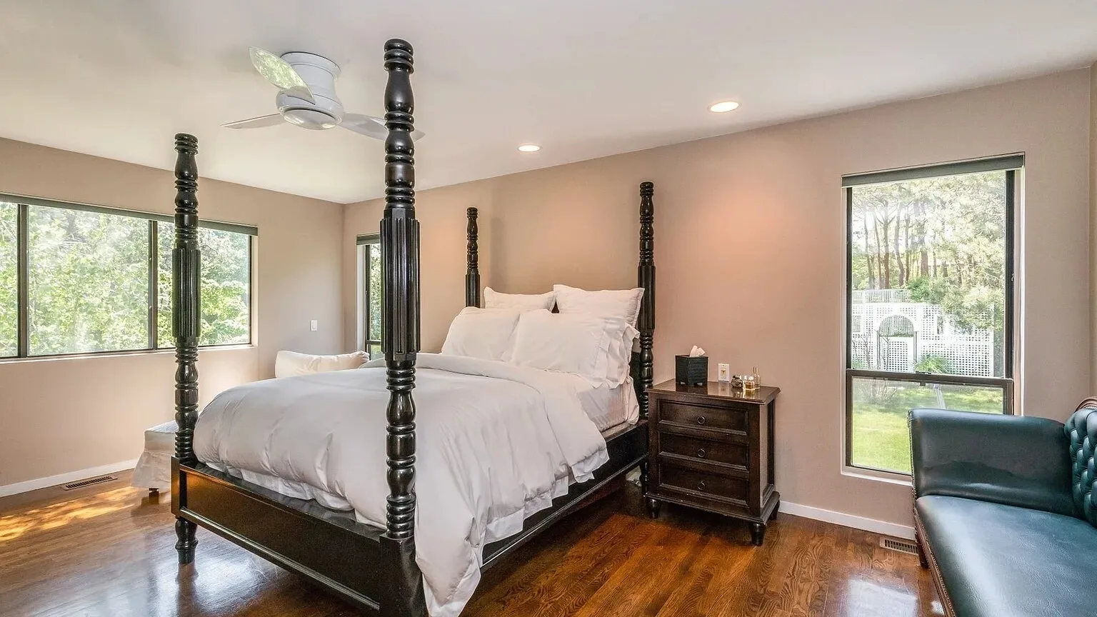 Un dormitorio con una cama con dosel oscuro, ropa de cama blanca y ventanas.