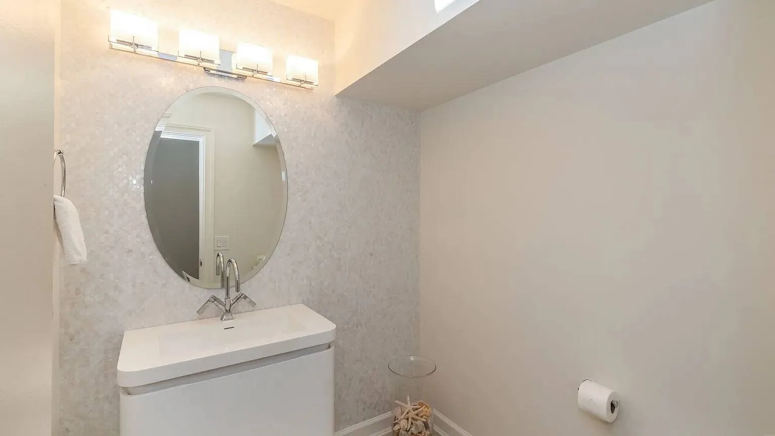 Un tocador de baño con espejo ovalado y luz sobre la pared.