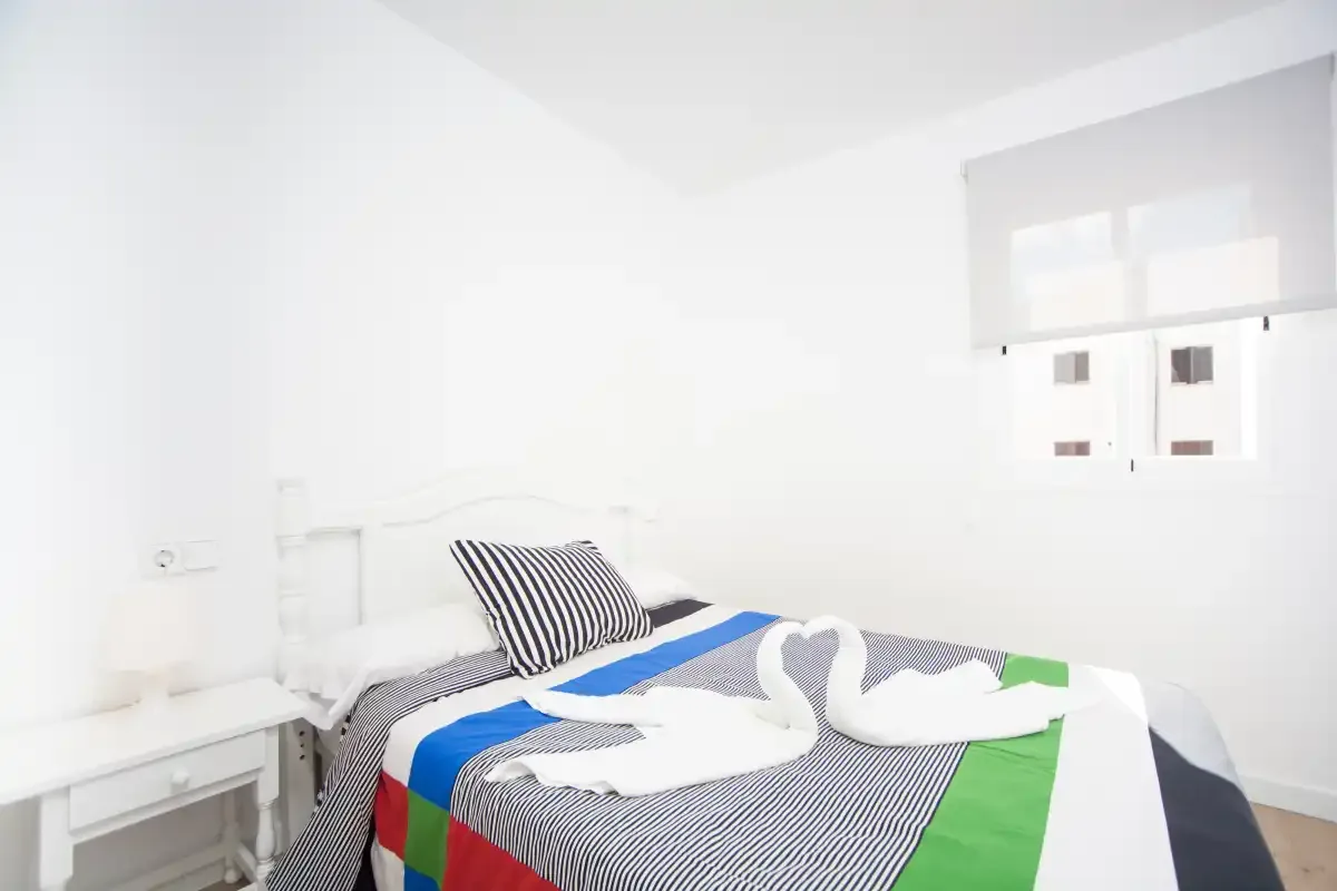 Un dormitorio luminoso con una cama cubierta de ropa de cama a rayas de colores.