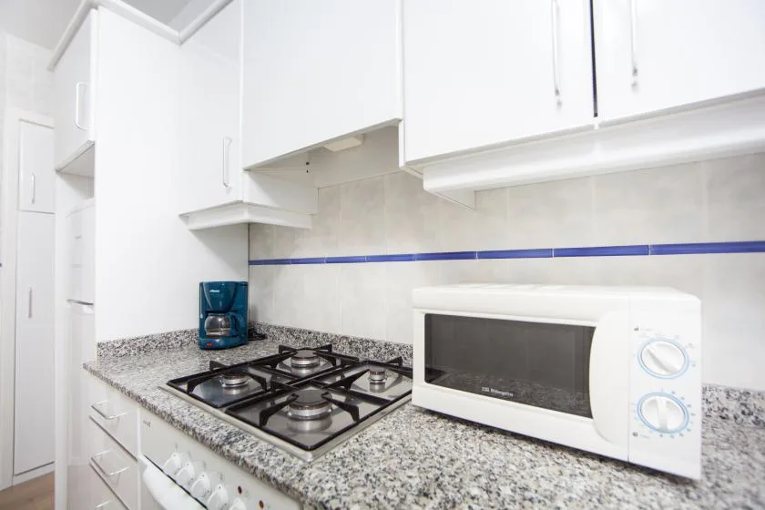 Una encimera de cocina luminosa tiene una estufa de gas y un microondas bajo armarios blancos.