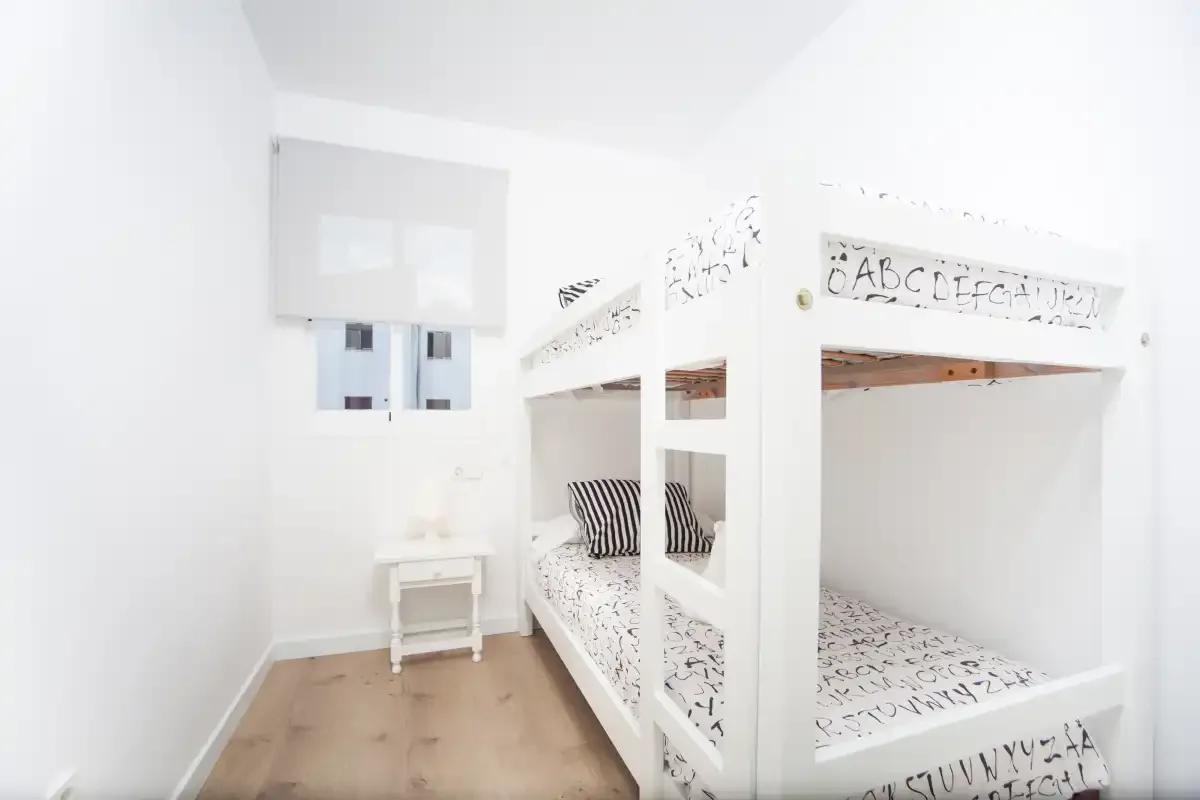 Un dormitorio luminoso con una litera blanca y una mesita de noche.