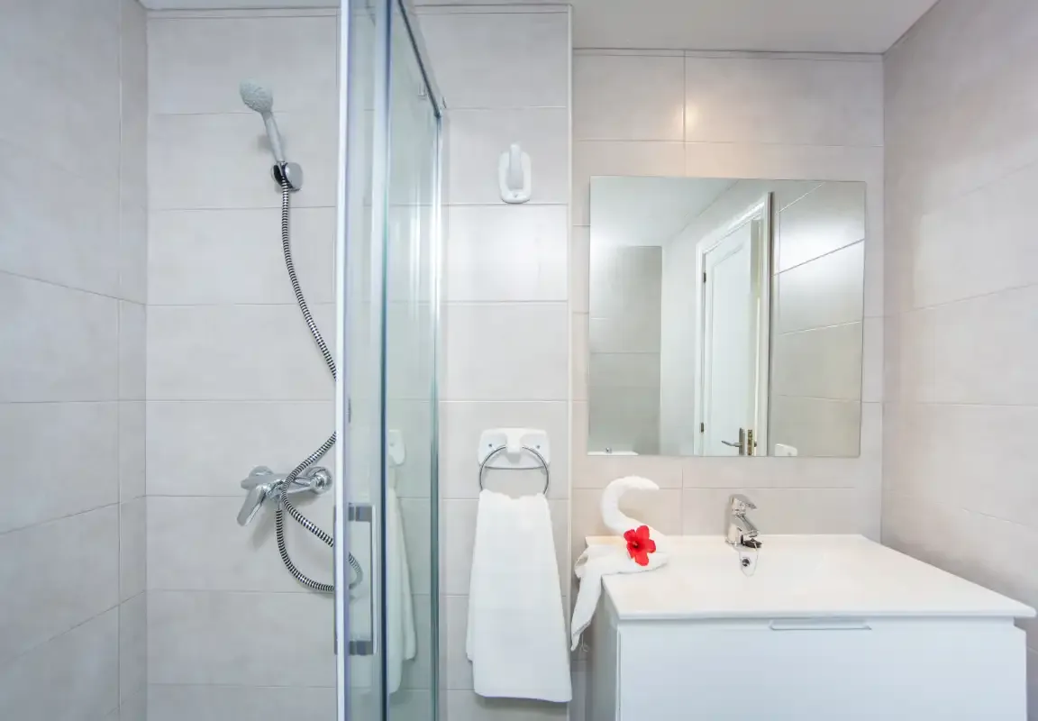Un baño luminoso con una ducha de cristal y un lavabo bajo un espejo.