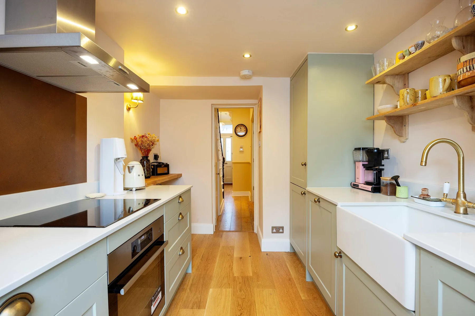 A galley kitchen with white counters, open shelves, and wood flooring.