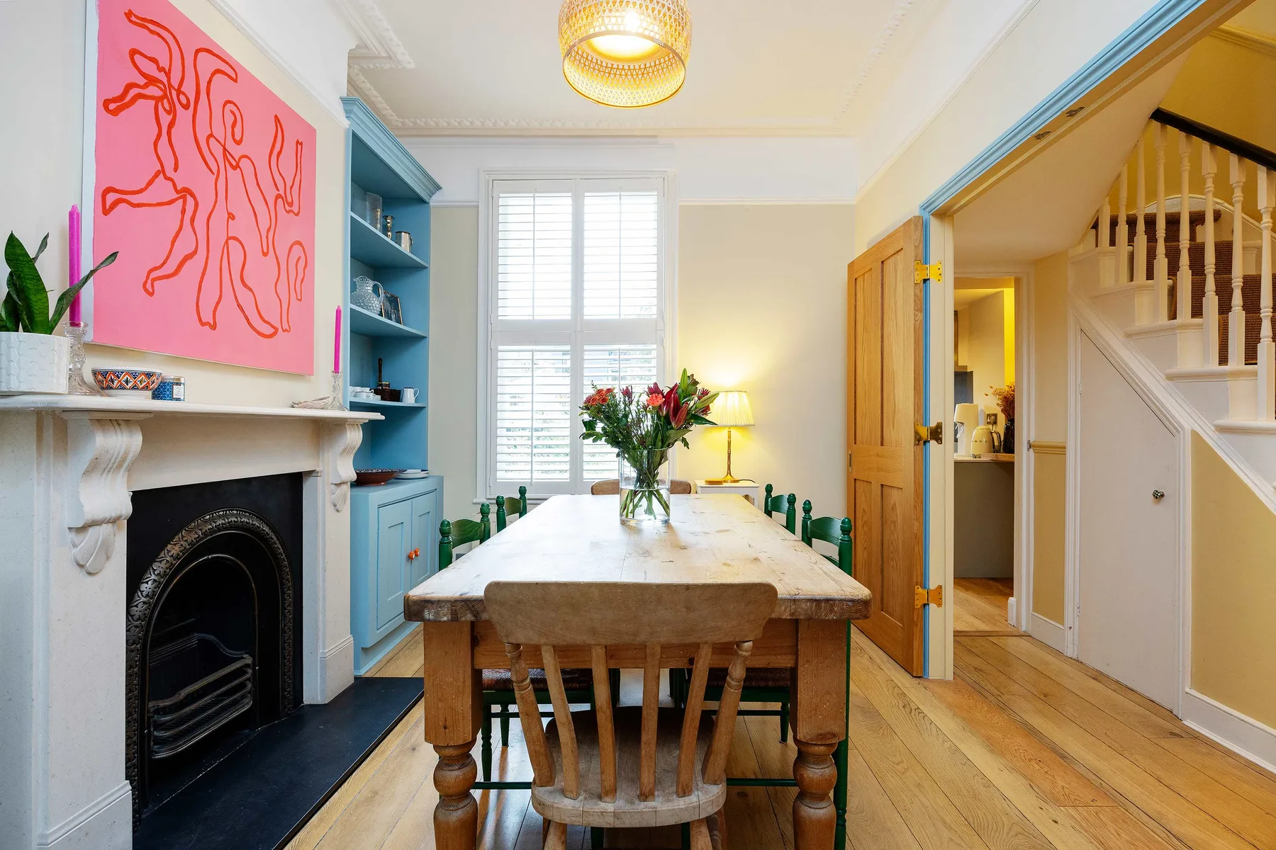 A dining room with a wooden table, colorful artwork, and a fireplace.