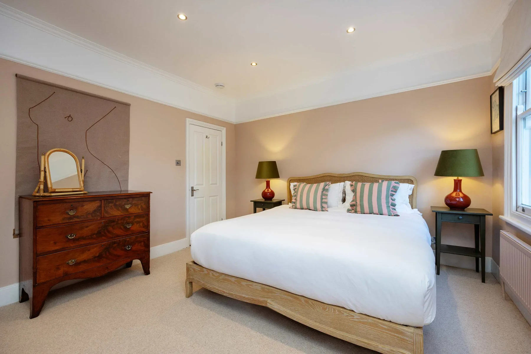 A bedroom with a neatly made bed, bedside tables, and a wooden dresser.