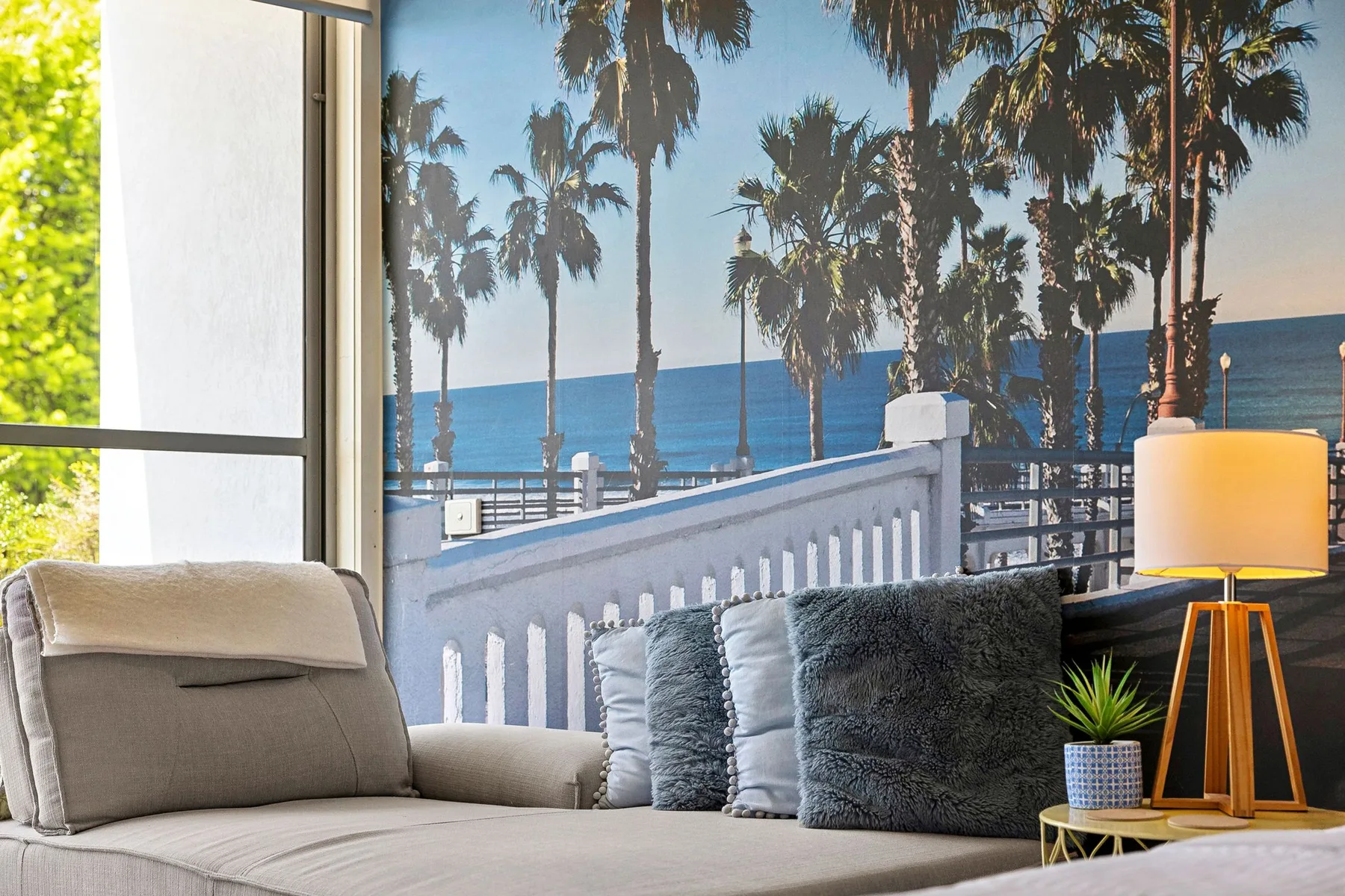 A seating area faces a palm-lined seaside view through a large window.