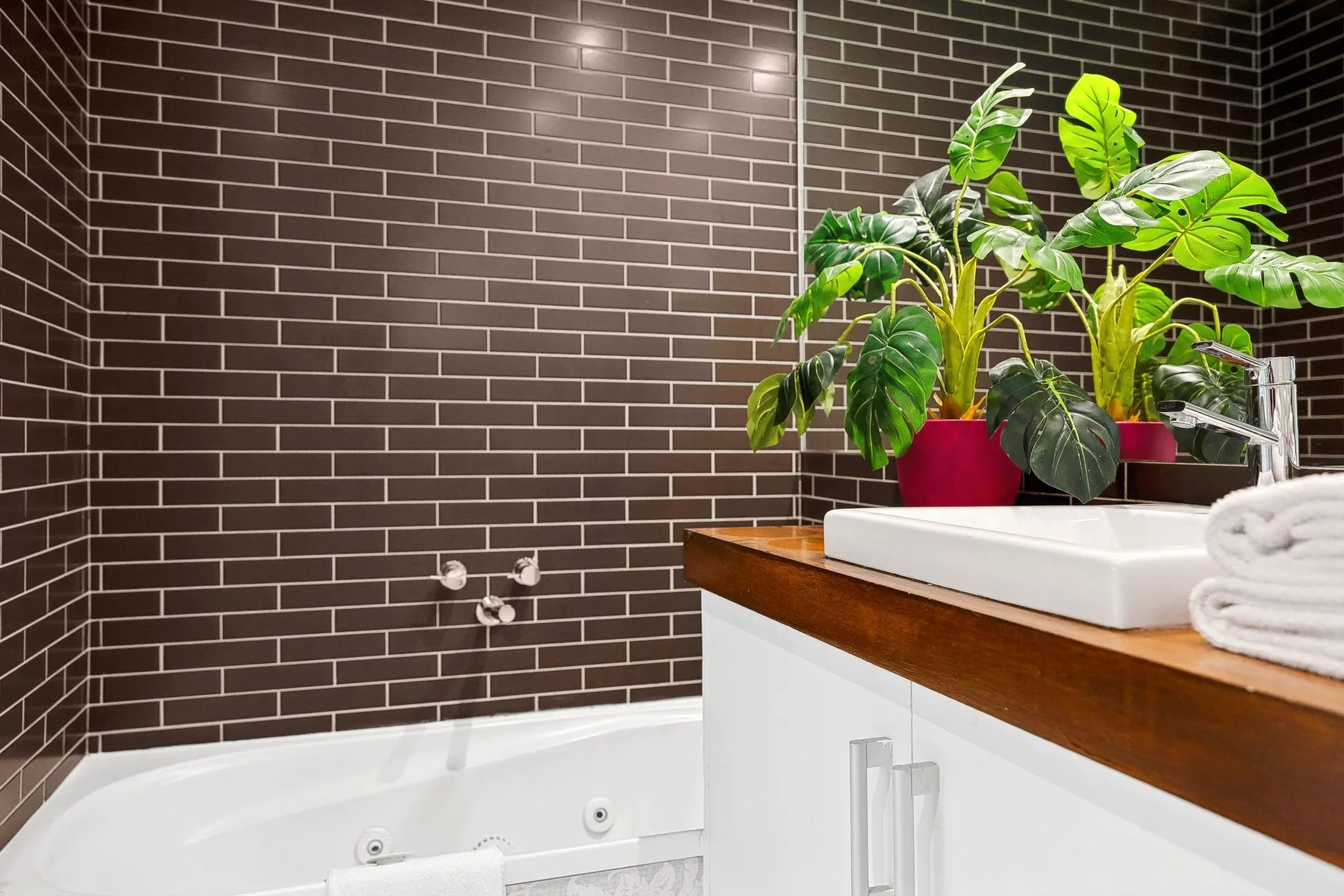 A bathroom vanity with a white sink and green plants against a tiled wall.