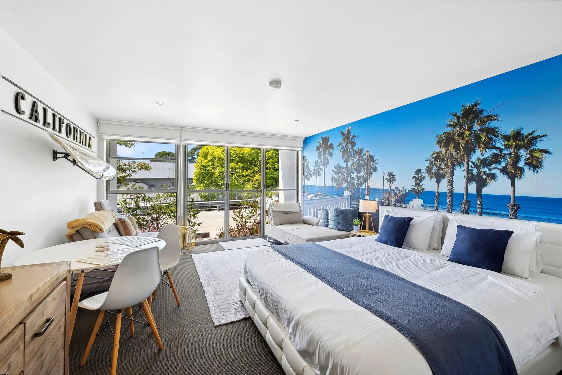 A bright bedroom with a large bed, seating area, and palm-tree mural.