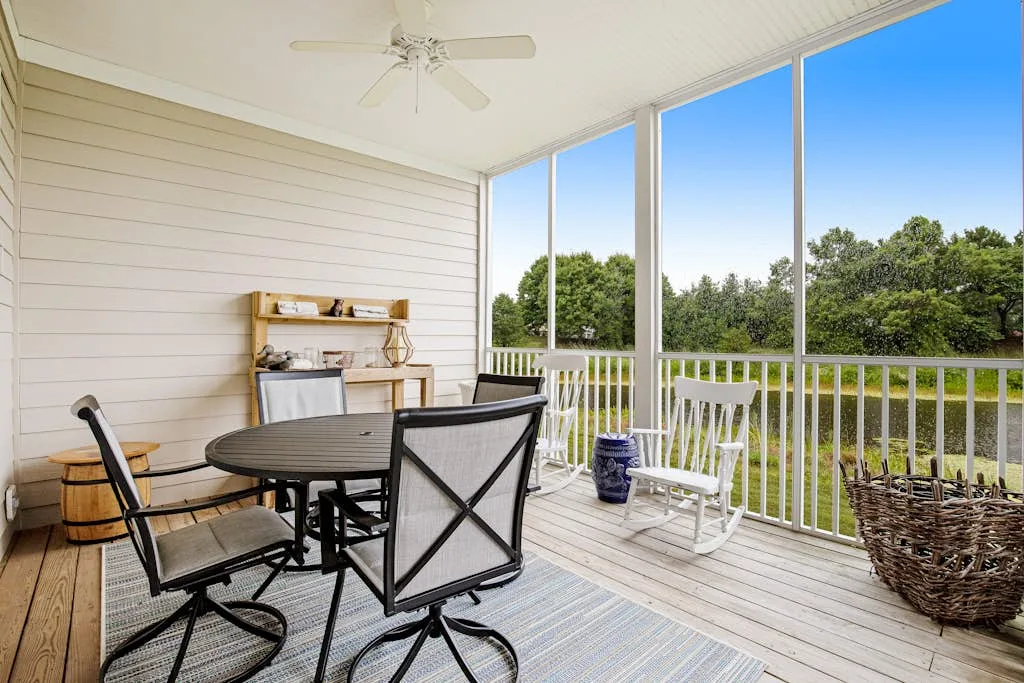 A screened-in porch with a dining table and rocking chair overlooking trees.
