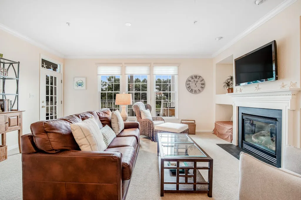A bright living room with seating, a glass coffee table, and a fireplace.