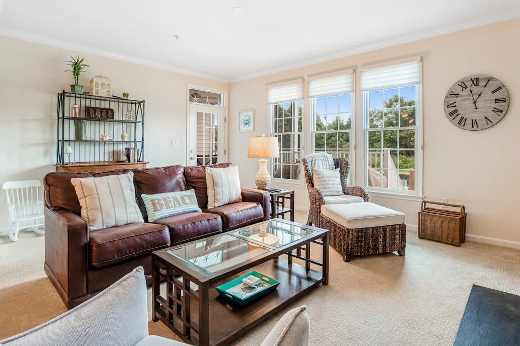 A bright living room with a leather sofa, glass coffee table, and large windows.