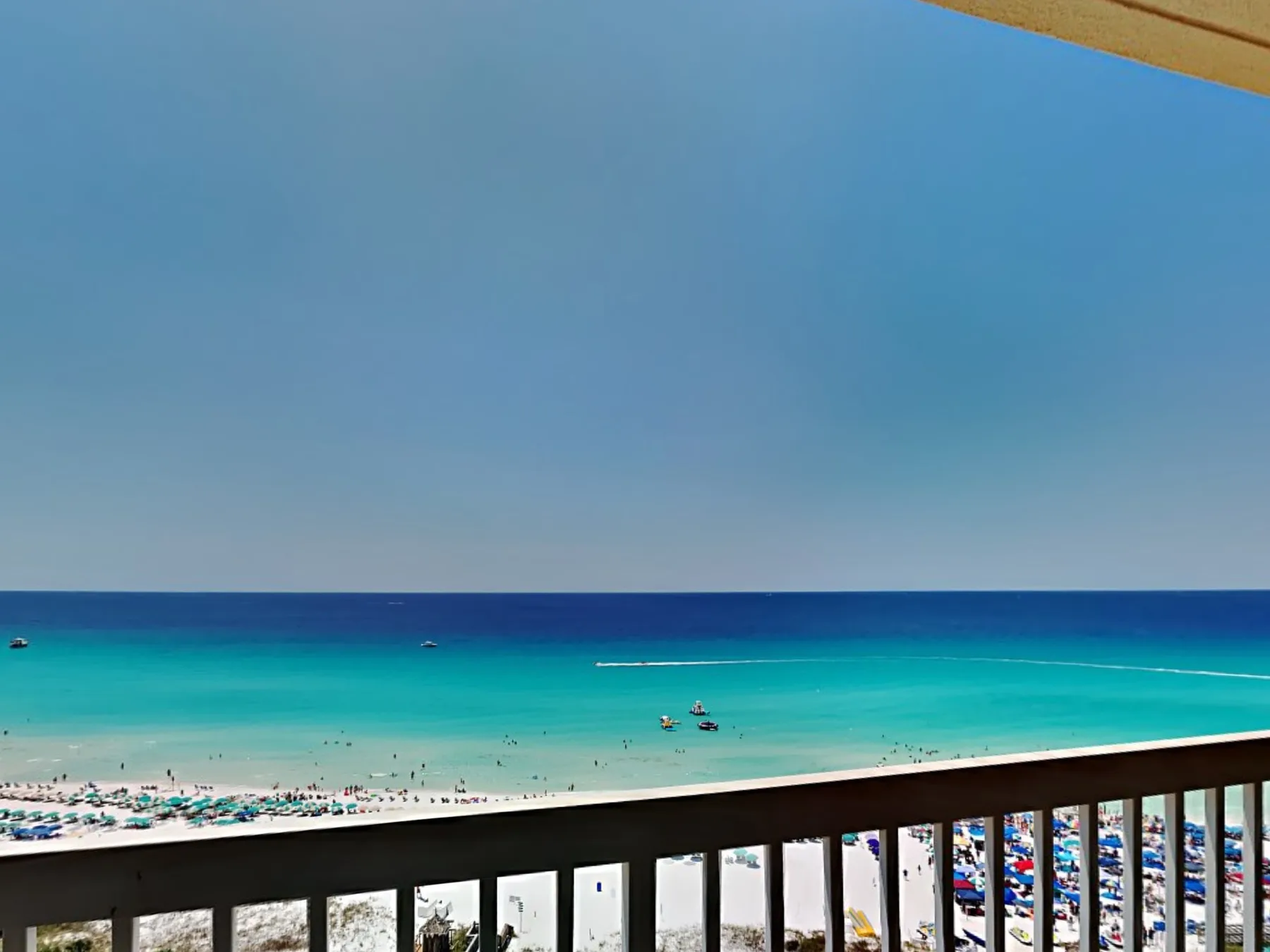 A beach and turquoise sea are visible beyond a balcony railing.