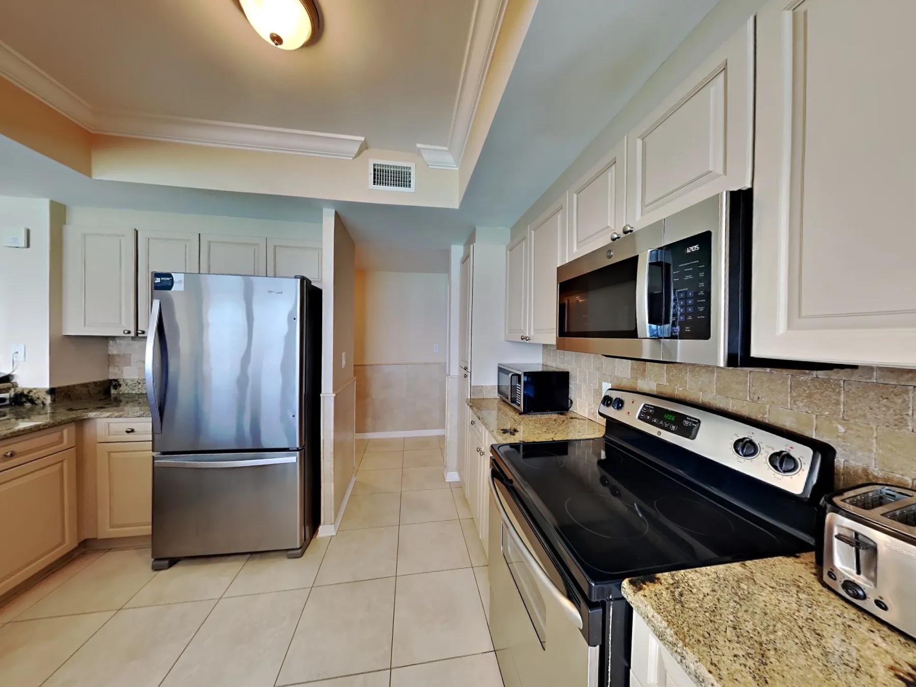 A bright kitchen with white cabinets, stainless steel appliances, and stone countertops.