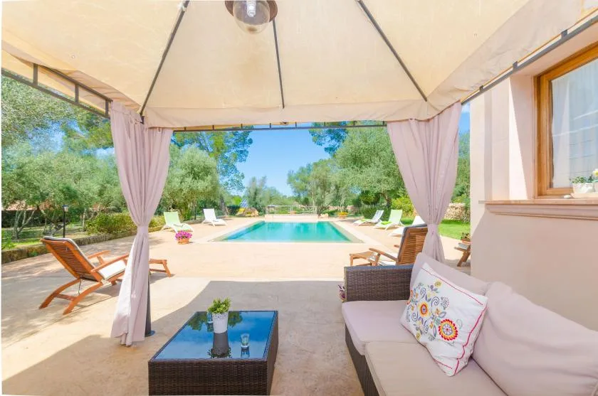 A shaded outdoor seating area opens onto a swimming pool and garden.
