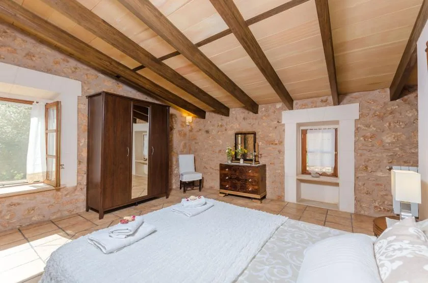 A bedroom with a large bed, wooden wardrobe, and exposed ceiling beams.