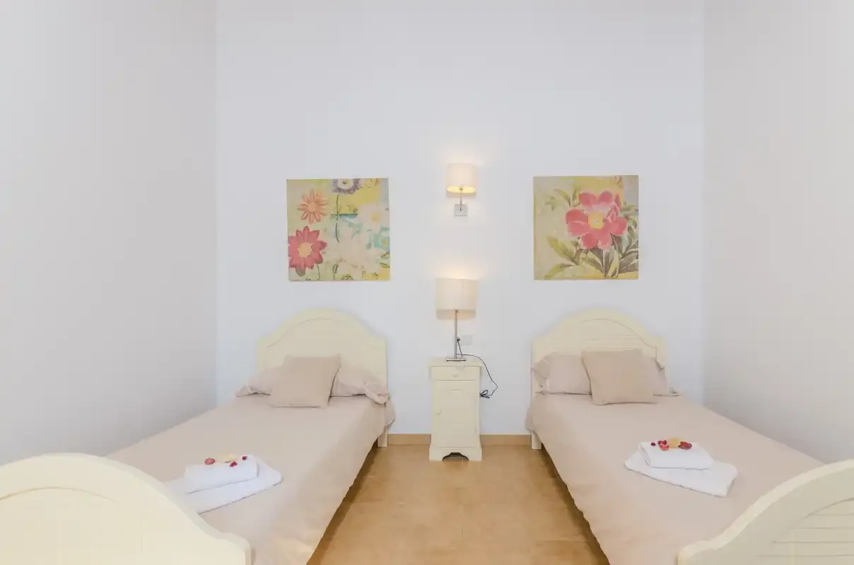 A bright bedroom with two single beds and floral wall art.