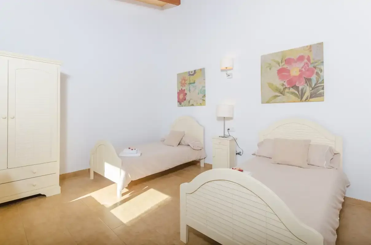 A bright bedroom with two beds and floral artwork on the wall.
