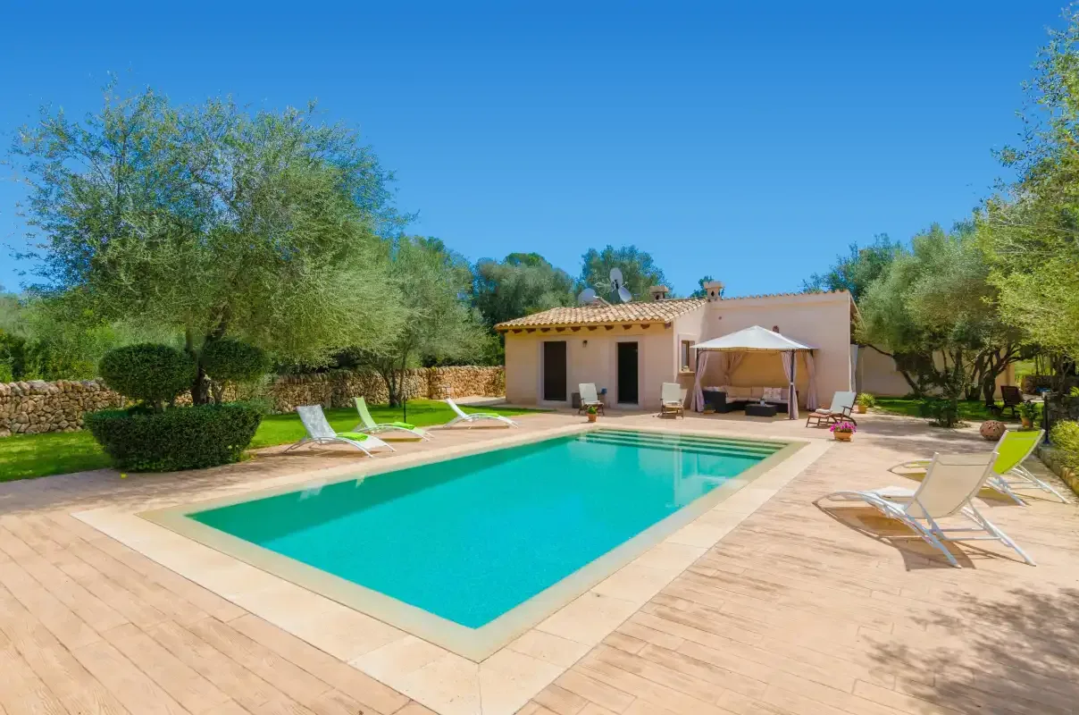 A swimming pool and paved patio sit beside a single-story building in a landscaped yard.