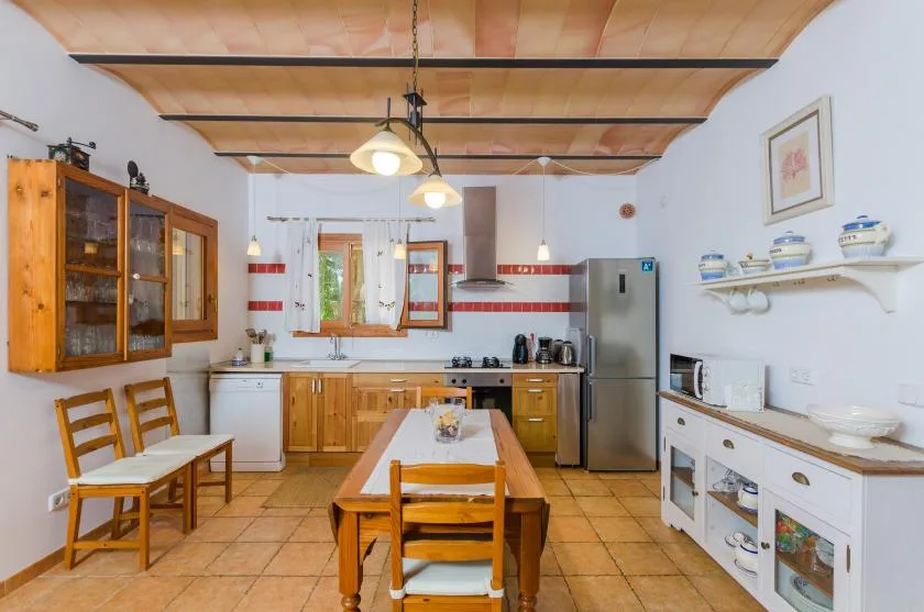 A rustic kitchen with wooden cabinets, a dining table, and a refrigerator.