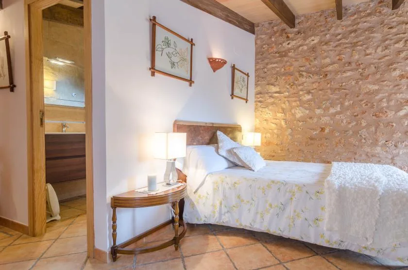 A bedroom with a bed beside a stone wall and wooden ceiling beams.