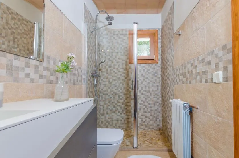 A tiled bathroom with a shower, sink, and small window.