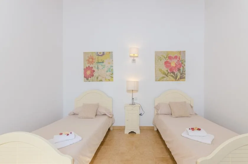 A bright bedroom with two single beds and floral artwork on the wall.