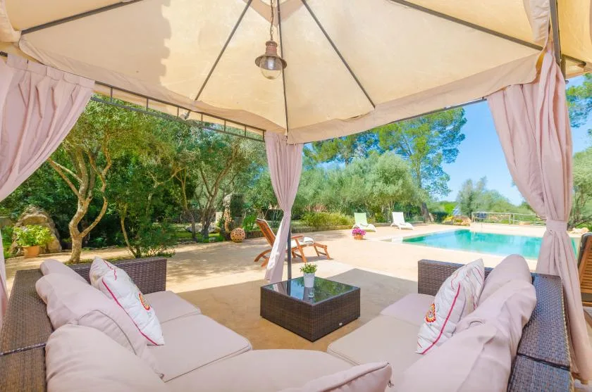 A shaded patio seating area overlooks a swimming pool and garden.