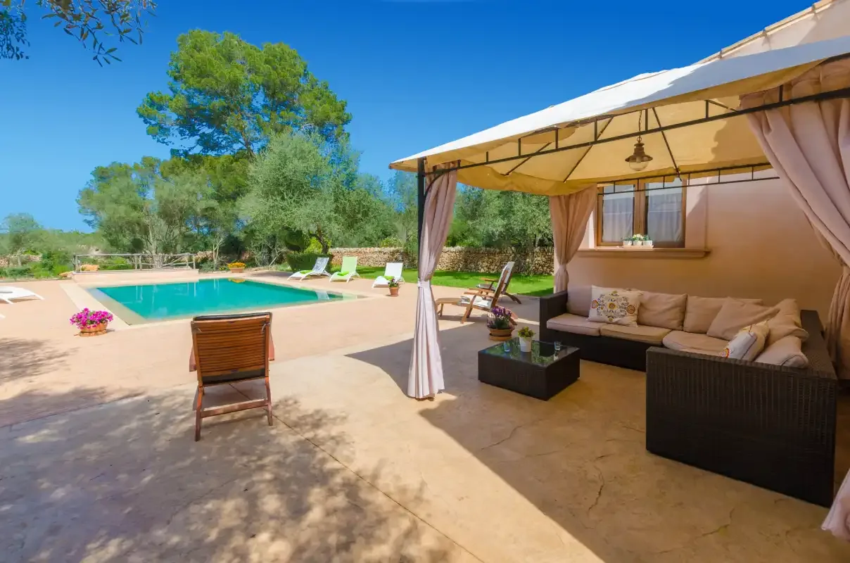 A shaded outdoor seating area beside a swimming pool and garden.