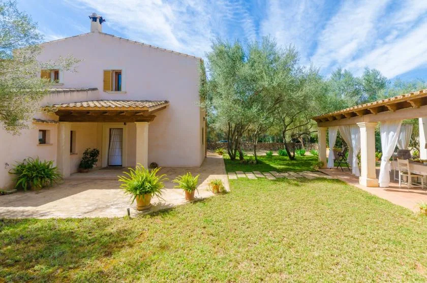 A house and covered patio overlook a sunny lawn and trees.