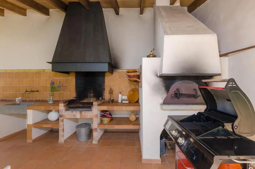 A rustic indoor cooking area with a large grill beneath exposed wooden beams.