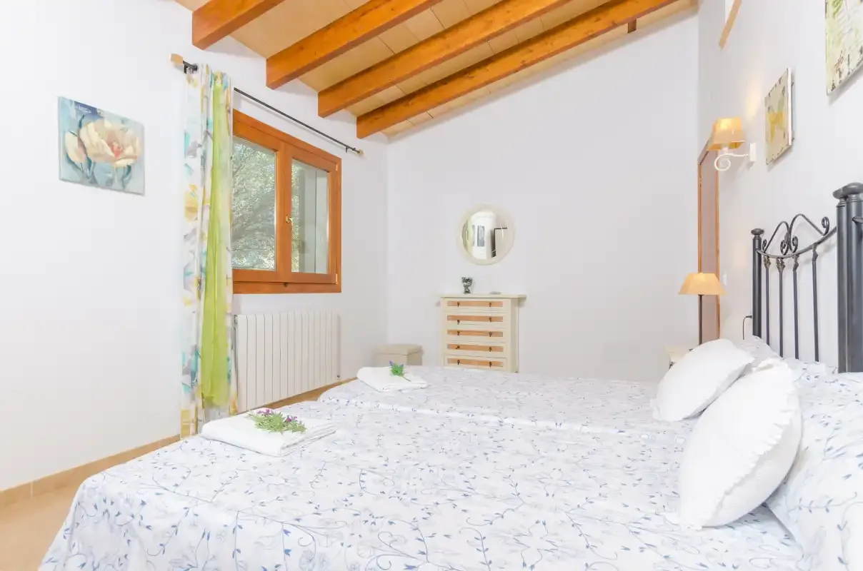 A bedroom with a bed beneath exposed wooden ceiling beams.