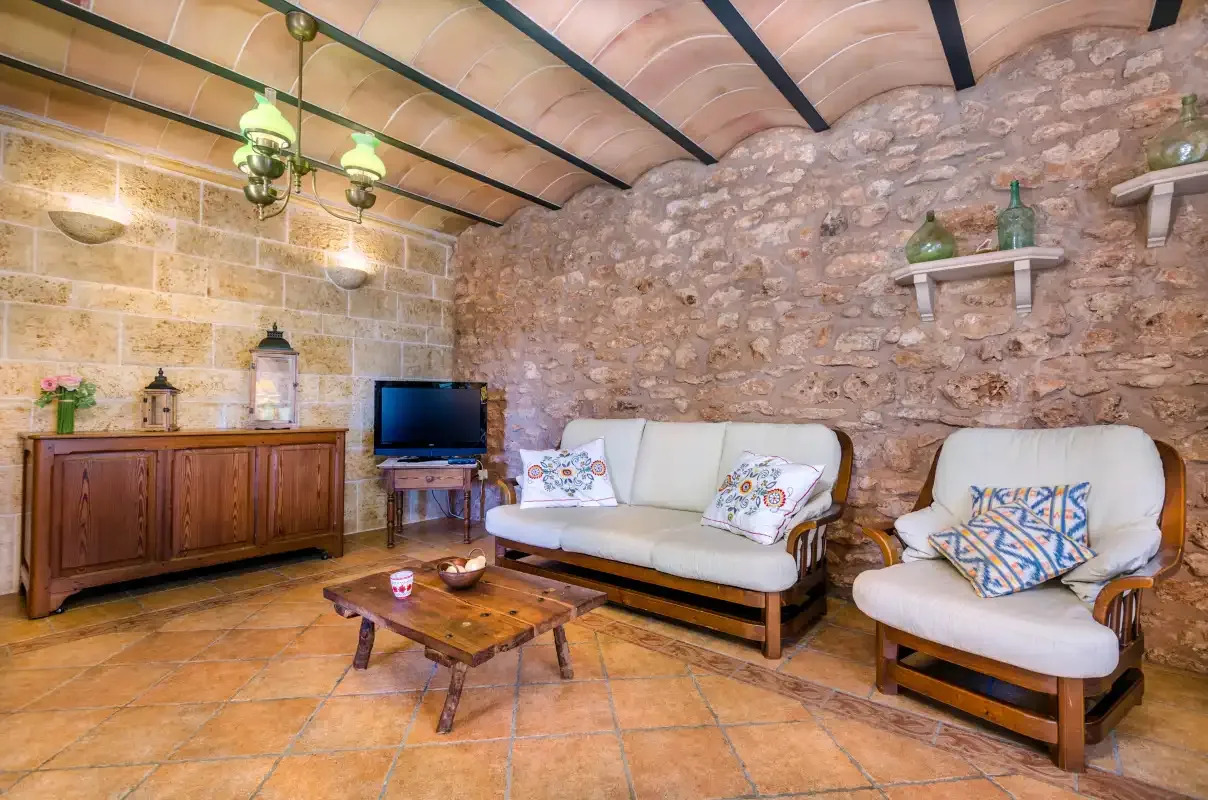 A rustic living room with light-colored seating, a wooden cabinet, and exposed stone walls.